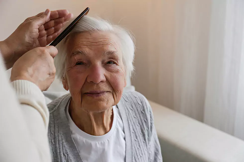 Pflegerin kämmt Patientin die Haare Pflegerin kämmt freundlich blickender Patientin die kurzen, weißen Haare